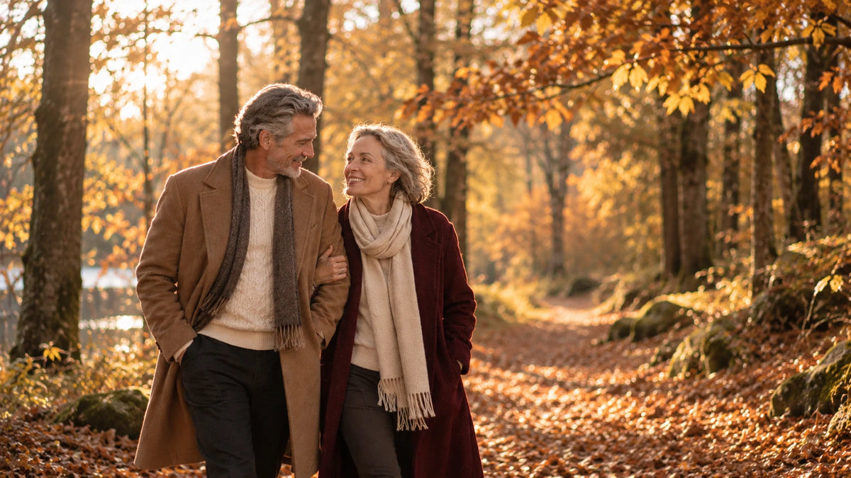 Couple élégant se promenant bras dessus bras dessous dans une forêt en automne, manteau camel et manteau bordeaux